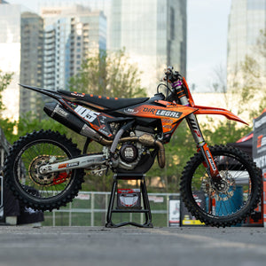 Orange and black dirt bike on a Risk Racing F.F.S. stand with cityscape in the background