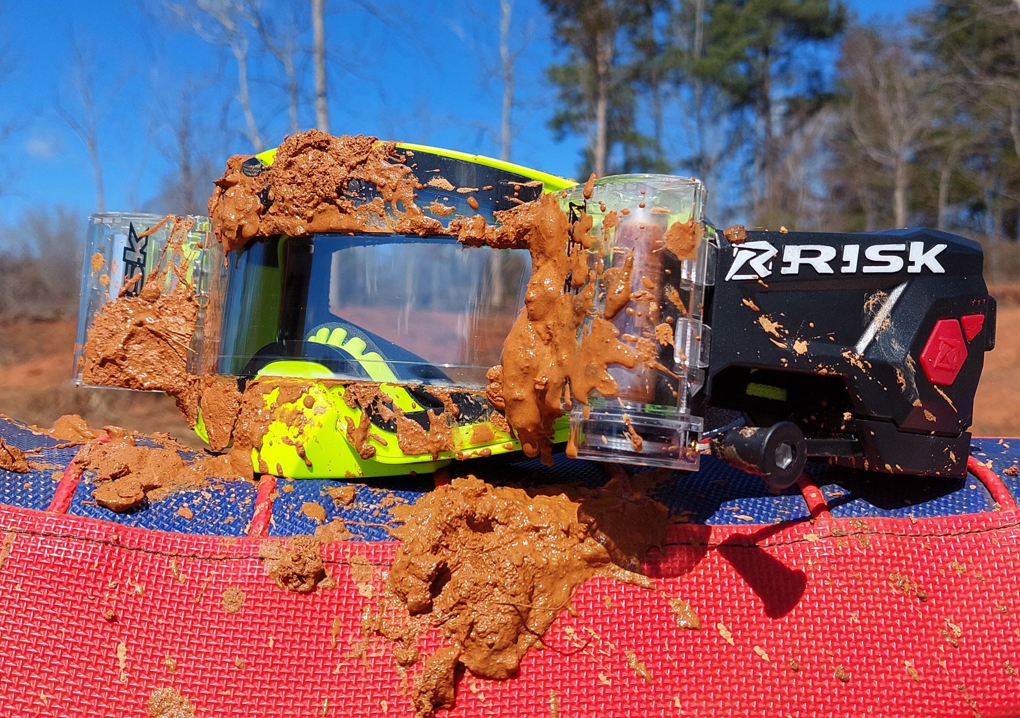 close up of Risk Racing's JAC Goggles with Ripper covered in Mud posing on a dirt bike seat